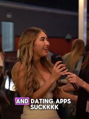 A woman with long blonde hair is holding a microphone and talking. The background is blurred, suggesting a social setting. Text overlay at the bottom reads "AND DATING APPS SUCKKK" in a stylized font and color.