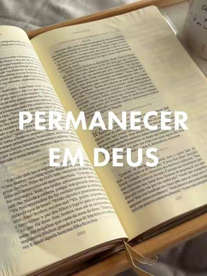 The cover image features an open Bible on a wooden stand, with a mug visible in the background. The pages of the Bible are filled with text, and the overlay text "PERMANECER EM DEUS" is prominently displayed. The image has a warm, inviting tone.