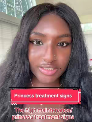 A selfie-style shot of a woman with long black hair and makeup, centered on her face. She is looking at the camera with a slight smile. A red banner with white text reading"Princess treatment signs" is placed just above a second text banner. The background is blurred, but appears to be indoors.