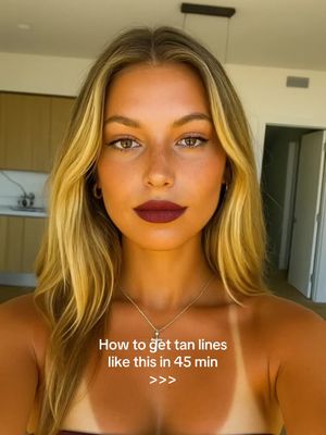 A selfie-style shot featuring a woman with blonde hair and dark red lipstick. She has a noticeable tan line on her chest. Text overlayed on image that read: "How to get tan lines like this in 45 min >>>"