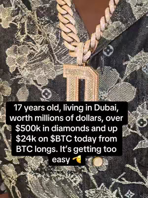 The image is a close-up of a person's chest area, focusing on a large, diamond-encrusted gold chain with a pendant. The pendant is in the shape of the letter 'D' also covered in diamonds. The person is wearing a patterned blue shirt and the background behind this is dark, possibly black.