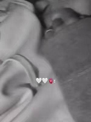 The photo is a black and white, out-of-focus image. Light colored fabric takes up most of the frame, with a person partially visible on the right side. At the bottom, there are three white hearts and a red heart, followed by two dots.