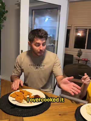 A man is seated at a table, appearing to address the camera. In front of him is a plate with food. A text overlay says, "I overcooked it".