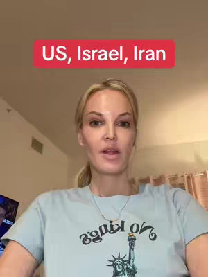 A woman with blonde hair and a light blue t-shirt is speaking to the camera. The text overlay reads "US, Israel, Iran". There's a necklace and the background seems to be of a home or room setting.