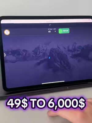 A tablet screen displaying a trading platform with a mountain range as a background. The screen shows various elements, including a balance of $49 and a 'TOP UP' button. Text overlaid on the image says '49$ TO 6,000$'. A hand is visible at the bottom providing context.