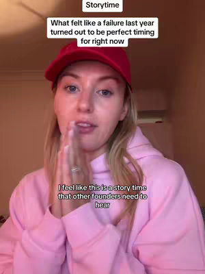 A woman in a pink hoodie and a red cap is looking at the camera, with a hand covering her mouth slightly. The background is blurred, with text overlays at the top and bottom.