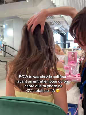 A person with brown hair is at a hair salon. A hand is touching their hair. The background has a retail element.