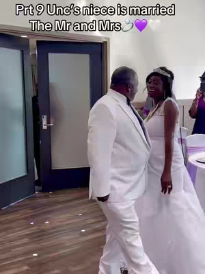 The cover image shows a wedding scene. A man in a white suit is seen from behind, seemingly escorting a woman in a white wedding dress. The woman, who is smiling and facing the man, has a tiara on her head. They are in a brightly lit room with doors on the background and tables with purple decoration.