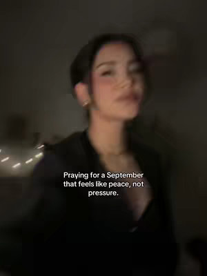 An out-of-focus image of a woman looking upwards and slightly to the side. She is wearing a black top, and the background is dark with some soft, diffused lighting. Text overlayed describes praying for a calmer month.