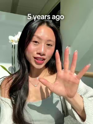 A woman with long black hair is smiling at the camera with her right hand raised, displaying five fingers, seemingly counting or signaling something. The text '5 years ago' is positioned above her head. She appears to be in a bright, naturally lit indoor space.
