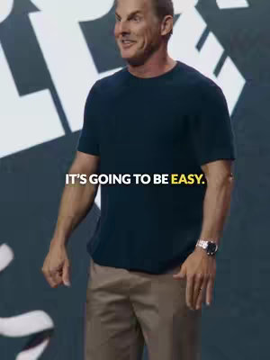A man in a dark blue t-shirt and khaki pants stands in front of a dark background. Text overlayed on the image reads "IT'S GOING TO BE EASY."