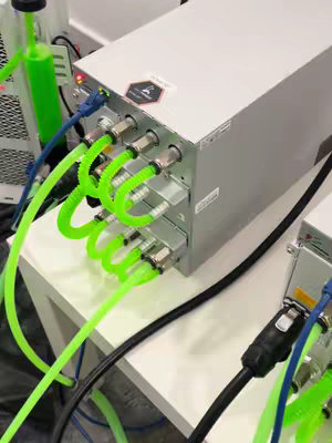Image of a hydro miner setup with cables, power supply, and tubing. The main focus is on a series of interconnected components, with vibrant green tubes providing cooling to the system. The setup is on a white surface, and a green accessory is nearby. The composition suggests a focus on the technology and function of the system.