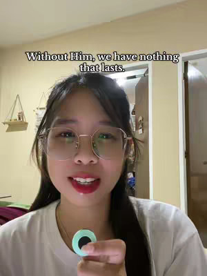 A woman with glasses smiles at the camera while holding a small, round object. Text overlays her head.