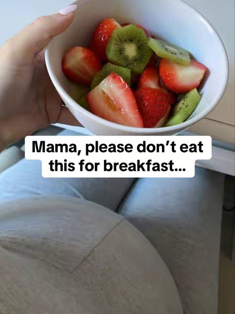 A hand holds a white bowl filled with sliced strawberries and kiwi. The image is taken from a slightly above angle, focusing on the bowl and the hand. Below, a woman's pregnant belly is visible, covered in gray material. Overlayed on the image is text that reads: “Mama, please don’t eat this for breakfast…”. The lighting is bright and natural, with a soft focus on the background outside the bowl.