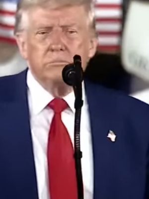 The cover image features a medium shot of former U.S. President Donald Trump standing behind a black microphone. He is wearing a navy blue suit, a white shirt, and a red tie. His expression is serious, and he is looking slightly off-camera. A small American flag pin is visible on his lapel. The background is out of focus, suggesting the setting of a speech or public appearance.