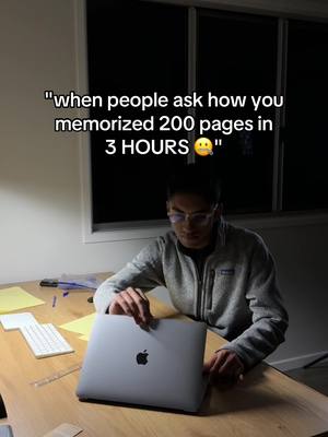 A person in glasses, wearing a gray hoodie, is sitting at a desk and holding up a laptop. The screen of the laptop is facing the viewer. There are papers, a pen, and a keyboard on the desk. The overhead text reads, "when people ask how you memorized 200 pages in 3 HOURS 😳".