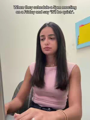 A woman is seated at a desk, appearing to work on a laptop. A text overlay is present at the top, while the woman is in focus, wearing a pink top and with a neutral expression.