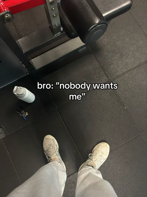 A first-person perspective shot, showing the lower body of a person in light-colored pants and sneakers standing on a black gym floor, looking down. A water bottle, a set of keys, and gym equipment are on the floor. Text overlay reads: "bro: 'nobody wants me'".