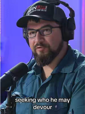 A man wearing a hat and headphones is in front of a microphone, speaking. The background is a blurry blue.