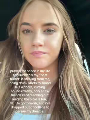 A selfie-style video featuring a young woman with long blonde hair. The woman is centered in the frame, and the background is blurred. She stares directly, with a serious expression.