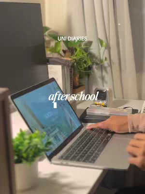 The image shows a laptop on a white desk with a small plant in a white pot. A person's hand is resting on the keyboard, and the laptop screen is displaying a blue-toned interface. Behind the laptop, a window with a curtain can be seen, along with more greenery. In the upper portion of the image text overlays say 'UNI DIARIES' and 'after school'.