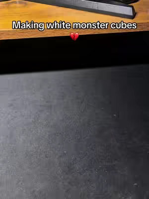 The cover image is a top-down shot of a black surface, likely a countertop or tabletop. A wooden surface is visible in the background. The text overlay says 'Making white monster cubes' in white text, with a broken heart emoji. It's a simple composition, with a focus on the textures and the text.