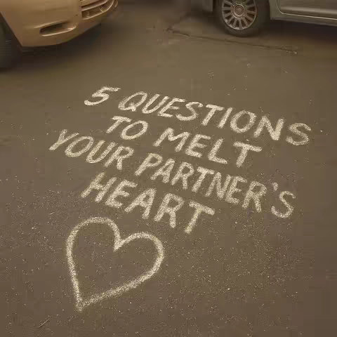 A top-down view shows text and a heart shape drawn in white chalk on a dark gray, asphalt-like surface. The text reads '5 QUESTIONS TO MELT YOUR PARTNER'S HEART'. Partial views of two vehicles are visible in the background, suggesting the artwork is outdoors.