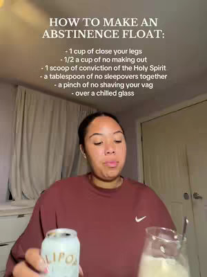 A young woman with dark hair and fair skin stands in front of a partially visible closet. She is wearing a maroon sweater with a small white Nike logo. She holds a can of OLIPOP in her left hand and a glass containing a light beige liquid in her right hand, looking slightly down. The background is a bedroom setting, with a white curtain to the left and a closed white wardrobe.