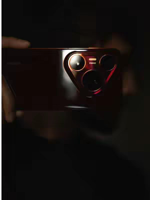 The cover image showcases a close-up of the back of a smartphone, likely a Huawei model, in a dark setting. The phone is held at an angle by unseen hands, and the focus is on the camera array, which has a distinctive circular design with multiple lenses. The phone has a dark, possibly burgundy finish. The lighting is dramatic, with bright illumination around the camera lenses, creating a high-contrast effect. The background is completely dark, emphasizing the phone's features. The composition is clean, with the phone taking up a significant portion of the frame.
