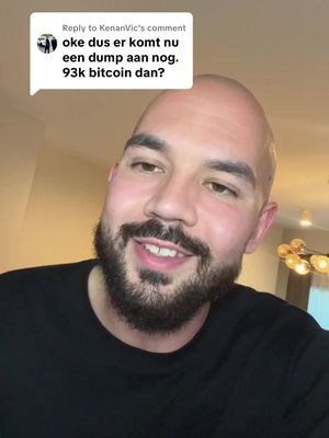 A medium shot of a man with a bald head and a full beard, wearing a black shirt. He is looking at the camera and smiling. In the top left corner, there is a comment section style text overlay with the text in Dutch.