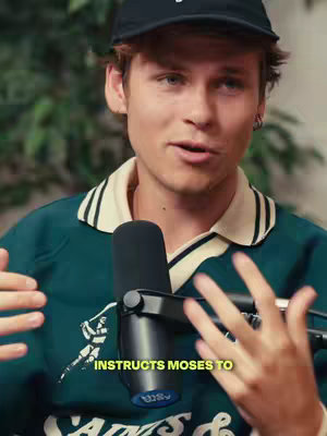 A young man with light skin, wearing a dark baseball cap and a green and cream polo shirt, speaks into a microphone. He has a short beard and is gesturing with both hands. Text across the bottom of the image reads: 'INSTRUCTS MOSES TO.' The background is blurred but seems to be indoors.