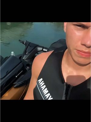 A man is seen partially in the image, appearing to be on a jet ski. The man is wearing a black life vest with the word 'AHAMAY' in white capital letters and a white stripe next to the writing across his chest. The foreground shows the black exterior of the jet ski.