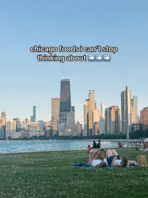 The image shows a vibrant cityscape with a clear sky. In the foreground, people are relaxing on green grass near a body of water. The text overlay reads 'chicago foods I can't stop thinking about...'
