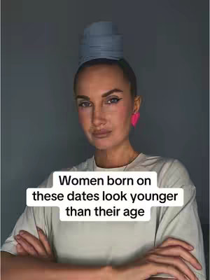 A woman with light skin, wearing a white t-shirt and pink heart-shaped earrings, is the central figure. Her arms are crossed. On her head is a cylindrical gray accessory. Framing her face is a gray backdrop. The text box at the bottom says, "Women born on these dates look younger than their age."