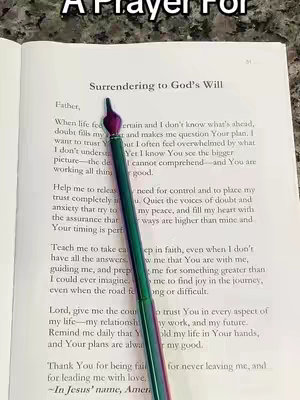 The image shows an open book on a light-colored surface, possibly a table. The book has a page open, with text visible. A pen with a colorful iridescent effect lies diagonally across the page. The focus is on the text, which has the heading "Surrendering to God's Will."