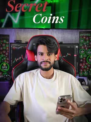 A man in a white t-shirt sits in a black and red gaming chair in front of computer monitors displaying stock charts. He holds a smartphone, with the text 'Secret Coins' overlaid above him.