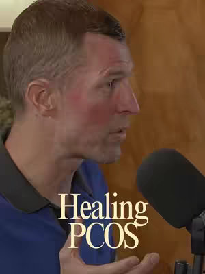 A medium shot features a man in profile, looking slightly towards the left. He has short, light-brown hair and a fair complexion with a slight flush to his cheeks. He wears a dark blue shirt with a black collar. In the foreground, just right, there's a black microphone. The background is a blurred wooden texture. The text "Healing PCOS" is superimposed on the lower-left side in a stylish, slightly distressed font.