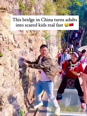 A man with a look of fear clings to the side of a rocky cliff, with a glass bridge in the background. Text indicating the bridge prompts fear. A woman in traditional clothing walks toward the background.