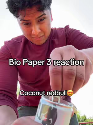 A young person with dark hair and a maroon shirt looks down with a slightly concerned expression. Their hands hold a can of Coconut Redbull, which is being opened. Text overlays the image, stating 'Bio Paper 3 reaction' and 'Coconut redbull' along with a heart-eyes emoji.
