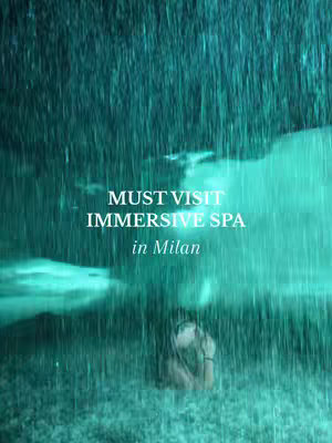 A turquoise-toned image features a figure standing amidst what appears to be a heavy downpour of rain, creating a blurred and watery effect. White text overlays the image, reading "MUST VISIT IMMERSIVE SPA in Milan."
