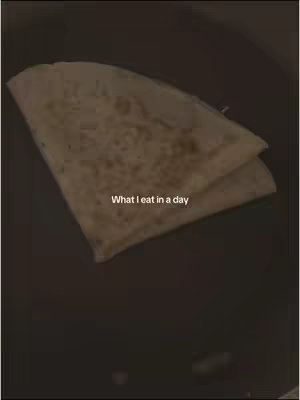 A close-up shot of a plate of food, likely a wrap or tortilla, partially folded. The dish sits centered against a dark, possibly black, surface. The lighting is dim, creating soft shadows.