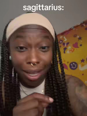 A close-up shot features a Black woman with long braided hair, wearing a beige headband and a nose ring, looking directly at the camera with a slight smile. Text "sagittarius:" is placed above her head. The background is a blurred mix of yellow and other colors.