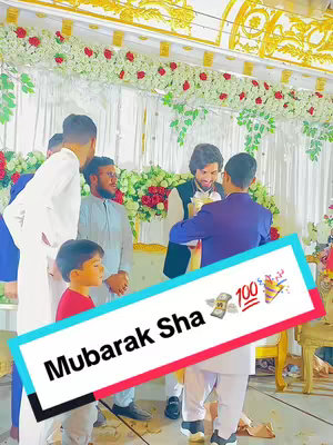 Image captures a celebratory event, likely a wedding or a similar joyous occasion, with multiple men dressed in formal attire and interacting near floral decorations indoors. The primary focus is on a man receiving a gift, symbolising a festive gathering. A graphic with text overlay adds a celebratory message to this image.