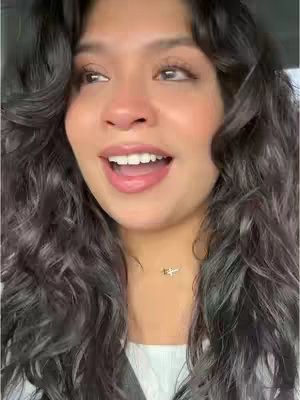 A close-up shot of a woman with long, curly dark hair, looking up and to the side with an open mouth, as if speaking or singing. Her face is the focal point, with her eyes and mouth clearly visible.