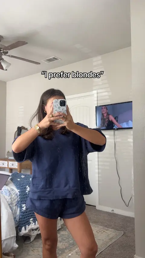 A person is taking a selfie in the mirror. The person is wearing a dark navy blue long sleeve shirt and matching shorts, with a gold watch and rings. The person is covering their face with a phone, with text in quotations overlayed onto the image.