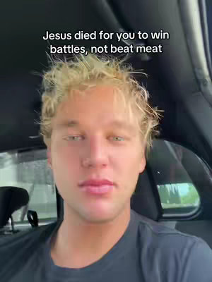 A close-up shot of a fair-skinned man with blond hair, looking directly at the camera. He's seated inside what appears to be a car, with the car's interior visible in the background. The image has text overlayed at the top, and the man is wearing a dark shirt.