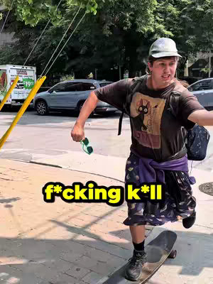 A person is skateboarding on a city street. The person is wearing a small hat, a dark t-shirt with a graphic, patterned skirt, and sneakers. They are rushing forward, holding green sunglasses. Yellow poles and a building are in the background, with a green and blue truck.