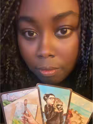 A close-up shot features a Black woman gazing directly at the camera with a neutral expression. Her hair is styled in long, braided twists. Below her, she holds three tarot cards. Each card displays an illustration with varied colors and themes.