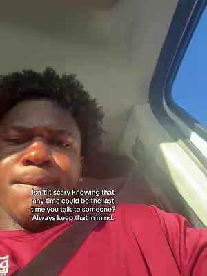 A close-up shot inside a vehicle. A person with curly black hair is the focus. The person is wearing a red shirt, and part of a seatbelt is visible. Text overlay is present.