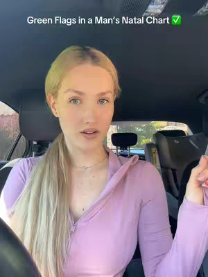 A woman sits in the driver's seat of a car. The background is blurred, but the interior has a car seat. The woman has long blonde hair and is wearing a pink long-sleeved shirt. Text overlayed on the image reads, "Green Flags in a Man's Natal Chart" with a green checkmark.